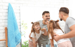 Father and daughter brushing teeth together in front of mirror