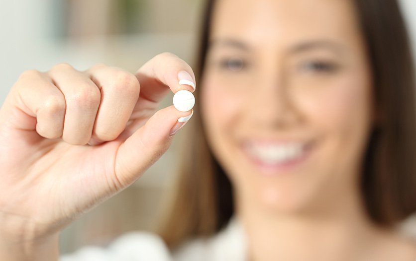 Smiling woman holding pill between fingers